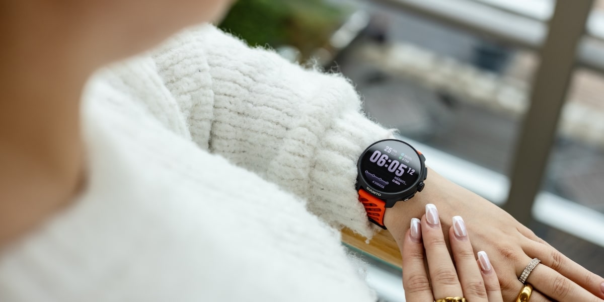 En person tittar på sin handled med Suunto Race 2 sportklocka som har en ljusstark skärm och ett orange armband.