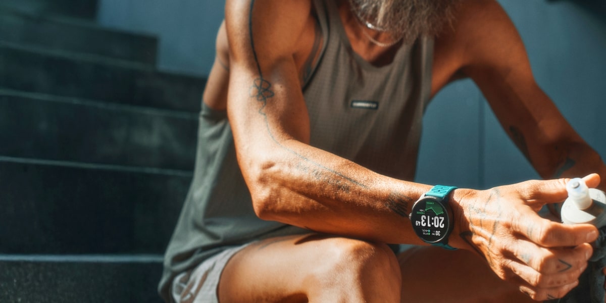 En löpare sitter på trappan och återhämtar sig, med Suunto Race 2 med grönt armband på handleden.