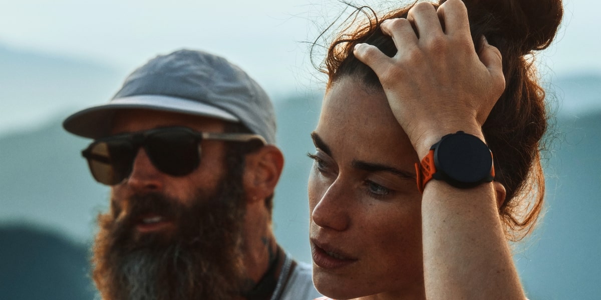 En friluftsentusiast stryker undan håret från pannan, med Suunto Race 2 med orange armband på handleden.
